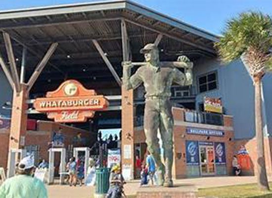 A large statue of a baseball player in front of the entrance to whataburger field, with people milling about.